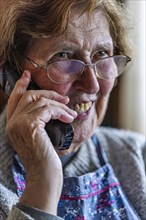 Laughing senior citizen with smock talking on the phone at home in her living room, Cologne, North