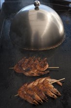 Spit-roasted prawns on a plancha, gas grill, stainless steel cooking bell in the back, Vandee,