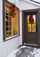 Window and brown front entrance door with illuminated Christmas lights and decorations on an old
