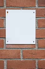 Blank white notice board attached to a brick wall with four screws, background with Copyspace