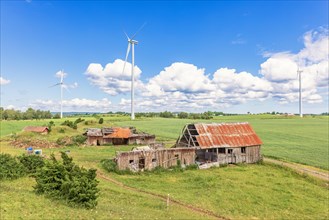 Landscape view at an old barn ruins in the countryside with high wind turbines on the fields