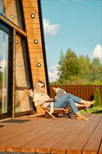 Woman typing on laptop while sitting in a folding wooden sun lounger on the terrace of a-frame