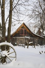 Old wooden rustic barn with red trimmed windows framed by trees in backyard garden in winter,
