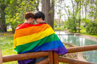 Rear view of a romantic scene of a multi-ethnic gay couple in love wrapped in lgbt flag embraced in