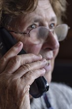 Senior citizen looks serious, frightened while talking on the phone in her living room, Cologne,
