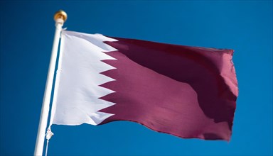 The flag of Qatar flutters in the wind, isolated against a blue sky