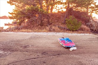 Small fiberglass boat beached on sandbar and tied to tree with sun setting in background in South