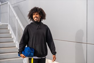 Sportive man with afro hairstyle walking next to stairs entering to a tennis court