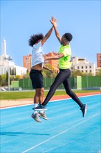 Vertical photo of two african american young friends jumping celebrating and clasping hands in a