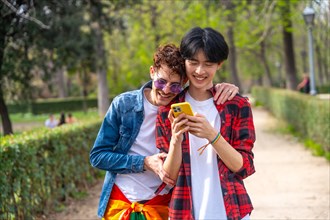 Frontal view of a multiracial young gay couple using phone in a park