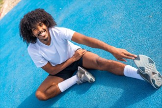 Sportive man with afro hairstyle warming up and stretching in an outdoor running track