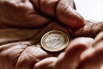 Euro coin in the wrinkled hand of a senior citizen, symbolising poverty and poverty in old age