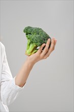 Healthy eating concept. Hand holds broccoli over grey background