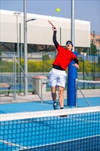 Vertical photo of a young sportive man jumping to reach the ball in a pickleball tennis court