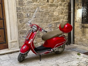 Red Vespa parked against an old wall on cobblestones, Trogir, Dalmatia, Croatia, Europe