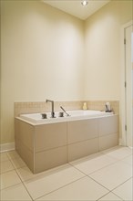 Soaking tub encased in a ceramic tile base in bathroom inside a renovated ground floor apartment in