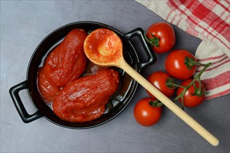 Whole tinned tomatoes in a pot, tomatoes and wooden spoon