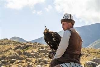 Traditional Kyrgyz eagle hunter riding with eagle in the mountains, hunting on horseback, near