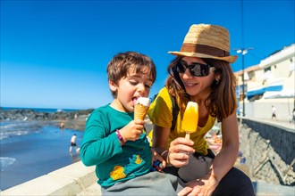 Mother with her little boy son enjoying summer vacation eating ice cream by the sea