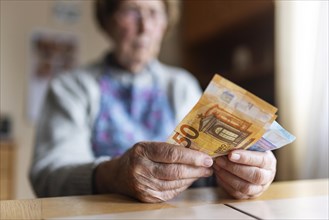 Senior citizen with wrinkled hands counts her money at home in her flat and holds banknotes in her