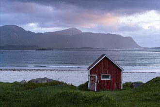 A red wooden hut on the sandy beach of Ramberg (Rambergstranda), with the sea behind it. At night