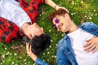 Top view photo of a multi-ethnic gay couple lying on the grass of a park together looking each