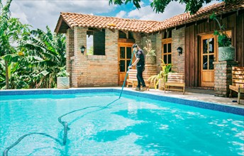 Maintenance and cleaning of home swimming pool with vacuum suction hose. Male worker cleaning a