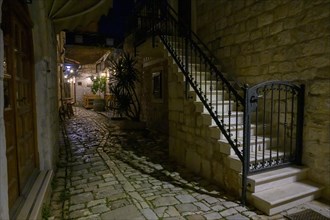 A narrow alley illuminated at night with alleyway lamp and outdoor seating of a restaurant, Trogir,