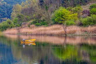 Small yellow metal fishing boat with small engine mount floating peacefully on a lake in South