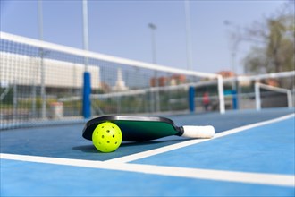 Horizontal photo of a pickleball ball and racket on the ground of a court with no people