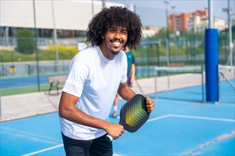 Portrait of a man with afro hairstyle smiling at camera having fun playing pickleball outdoors
