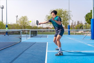 Side view of a young fit man playing pickleball in an outdoor court