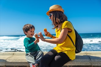 Mother with her little boy son eating ice cream by the sea on summer vacation