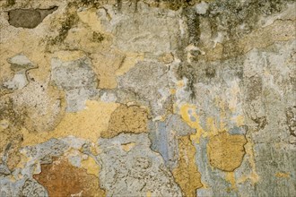 An old wall with peeling paint in various shades of brown, yellow and orange, background, texture