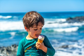 Child eating a delicious ice cream by the sea in summer. Family vacation concept