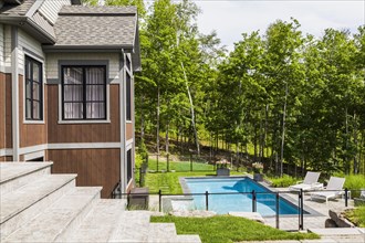 In-ground swimming pool and rear view of contemporary natural stone and brown stained wood and