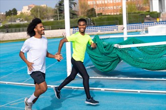 Two african american happy friends smiling while training in an outdoor running track