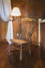 Spindle high back antique wooden rocking chair and lit pedestal lamp in hallway on upper floor