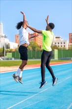 Excited running team of two african american young men jumping high-fiving in a running track