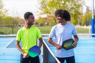Portrait of two african friends smiling face to face standing in a pickleball court