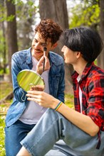 Vertical photo of two multi-ethnic gay men applying make up in a park