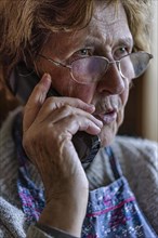 Senior citizen looks serious, frightened while talking on the phone in her living room, Cologne,