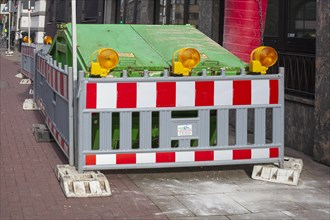 Construction site with barrier and waste container or skip for building rubble on a footpath,