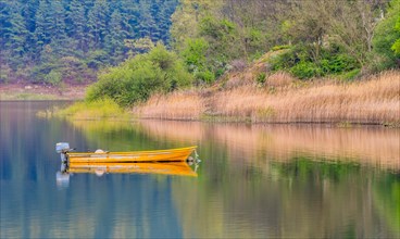 Small yellow metal fishing boat with small engine mount floating peacefully on a lake in South