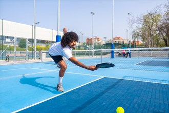 Full length photo of an african sportive man trying to reach the ball playing pickleball in an