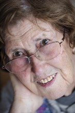 Portrait of a smiling senior woman with glasses in her living room, close-up, Cologne, North