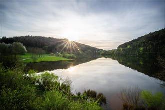 A lake in a landscape shot. A sunset and the natural surroundings are reflected in the water of the