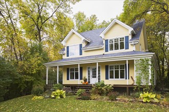 Two storey yellow clapboard with blue and white trim cottage style home facade in autumn, Quebec,