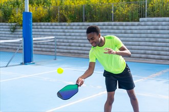 Horizontal photo with copy space of an african young man playing pickleball in an outdoor court
