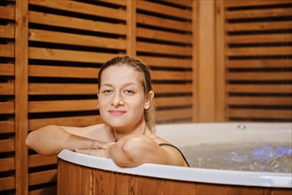 Smiling mid adult woman leaning on the edge of hot tub while evening relaxation in water